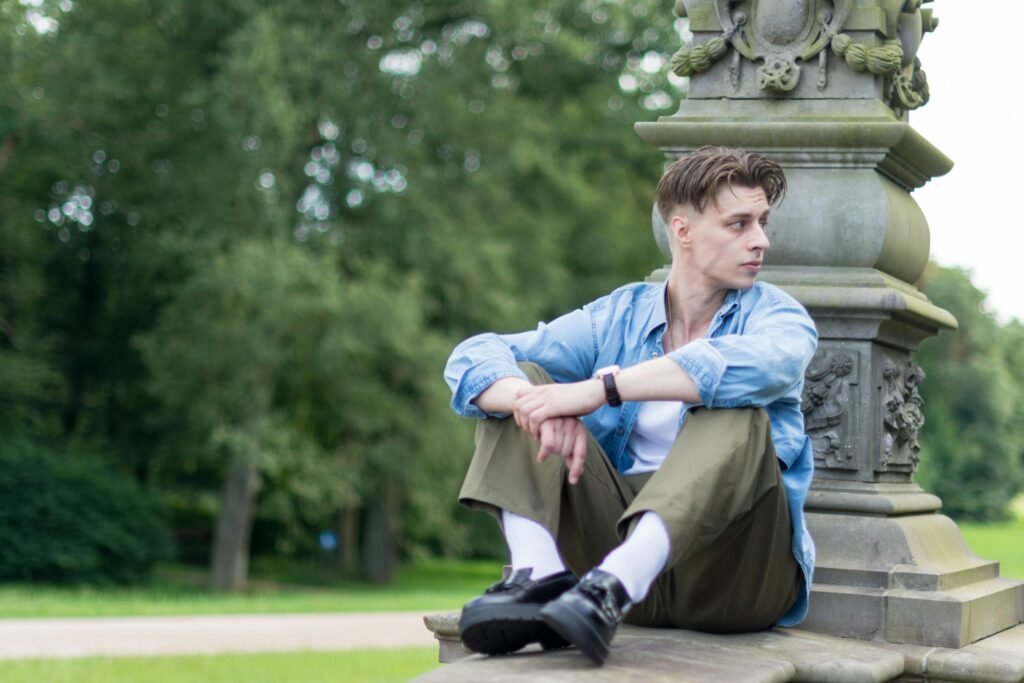 Young man sitting thoughtfully outdoors in a peaceful park, showcasing leisure and introspection.
